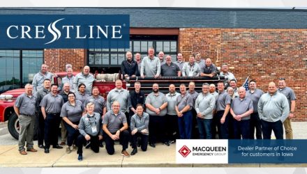 Group photo of the MacQueen Emergency Group team standing in front of a vintage red fire truck outside a brick building. The Crestline logo appears in the top left corner with a caption identifying MacQueen Emergency Group as the dealer partner of choice for customers in Iowa