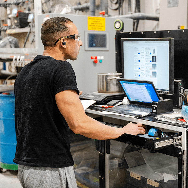 Crestline plant worker wearing safety glasses and earbuds reviews information on a computer screen at a workstation inside a manufacturing facility
