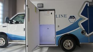 Side compartment of a Crestline ambulance shown open, revealing a spacious, illuminated storage area with LED lighting