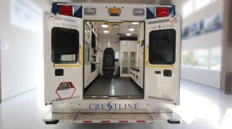 Rear view of a Crestline ambulance with both back doors open, showing the clean, organized interior with seating, storage cabinets, and medical equipment space