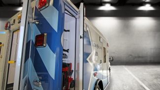 Rear side view of a Crestline ambulance with exterior storage compartment open, showing mounted stretcher and organized shelving