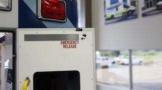 Close-up of the rear door of a Crestline ambulance showing the emergency release handle, marked with red text and an arrow for quick identification