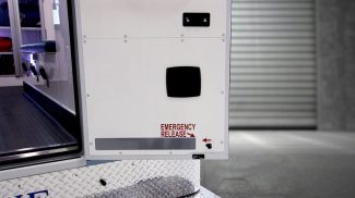 Close-up of the rear door of a Crestline ambulance showing the emergency release handle, marked with red text and an arrow for quick identification