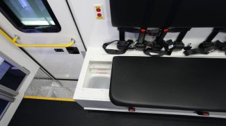 Interior of a Crestline ambulance showing a bench seat with seatbelts and integrated under-seat storage compartment for medical supplies