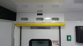 Interior side door of a Crestline ambulance featuring an overhead storage cabinet with yellow safety padding, and an emergency release handle