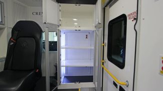 Interior of a Crestline ambulance showing a black attendant seat beside illuminated medical storage cabinets with adjustable shelves