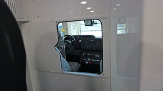 View through the interior partition window of a Crestline ambulance, showing the driver’s cab with the Ford steering wheel, dashboard, and mounted control panel