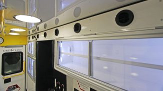 Interior of a Crestline ambulance featuring overhead LED dome lights, circular air vents, and large storage cabinets with sliding glass doors