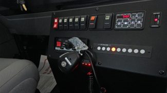Close-up view of a Crestline ambulance control panel with labeled switches, digital temperature display, intercom system, and handheld radio microphone