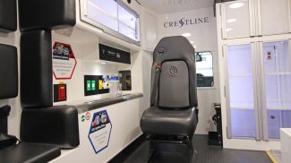 Crestline ambulance interior showing a black attendant seat with safety harness, adjacent storage cabinets, and mounted medical equipment
