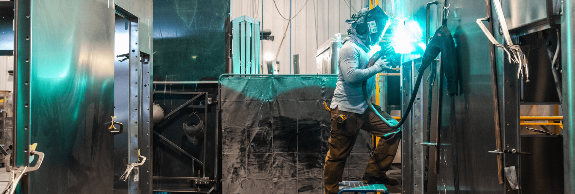 Plant worker wearing protective gear and a welding helmet using a welding torch on the outside of an ambulance inside the Crestline facility
