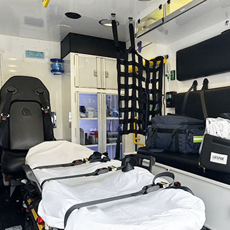 Interior of a Crestline ambulance with a stretcher, medical equipment bags, seating, and storage cabinets for emergency supplies