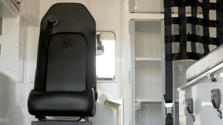 Interior of a Crestline ambulance showing a black attendant seat with seatbelt, storage cabinets, equipment mounts, and safety net separating compartments.