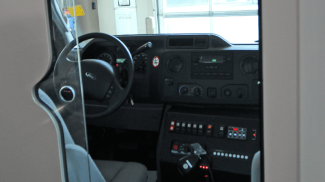 View through a partition window showing the driver’s cab of a Crestline ambulance, featuring the steering wheel, dashboard controls, and communication equipment