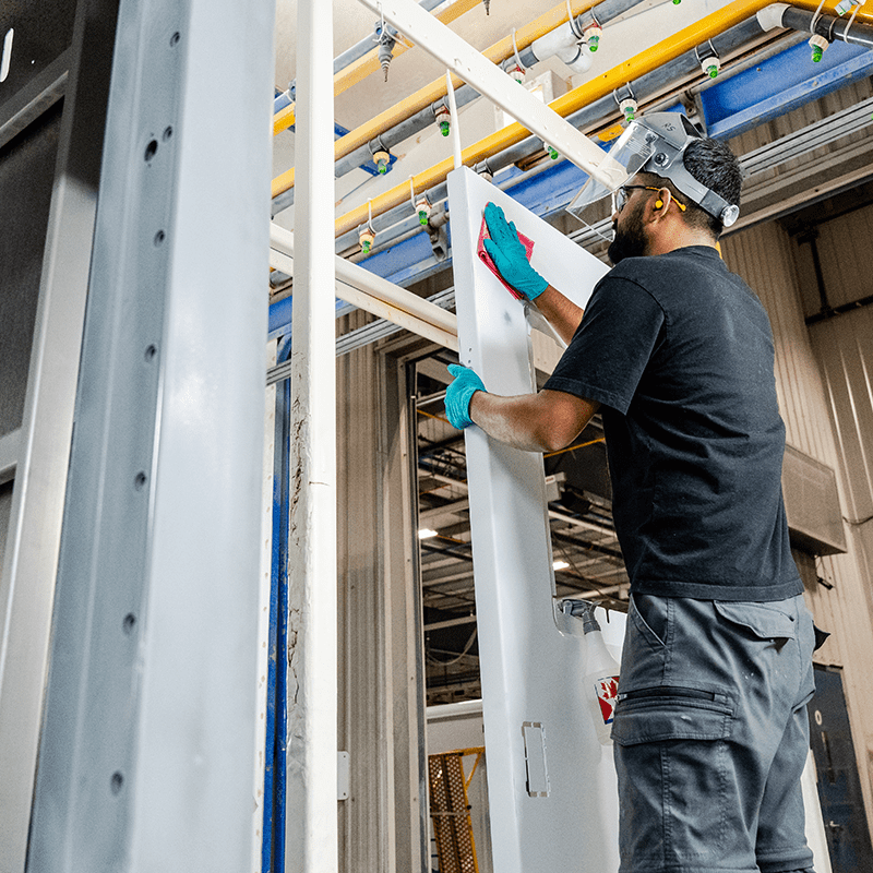 Crestline worker wearing safety goggles and gloves prepares an ambulance door for painting inside a manufacturing facility