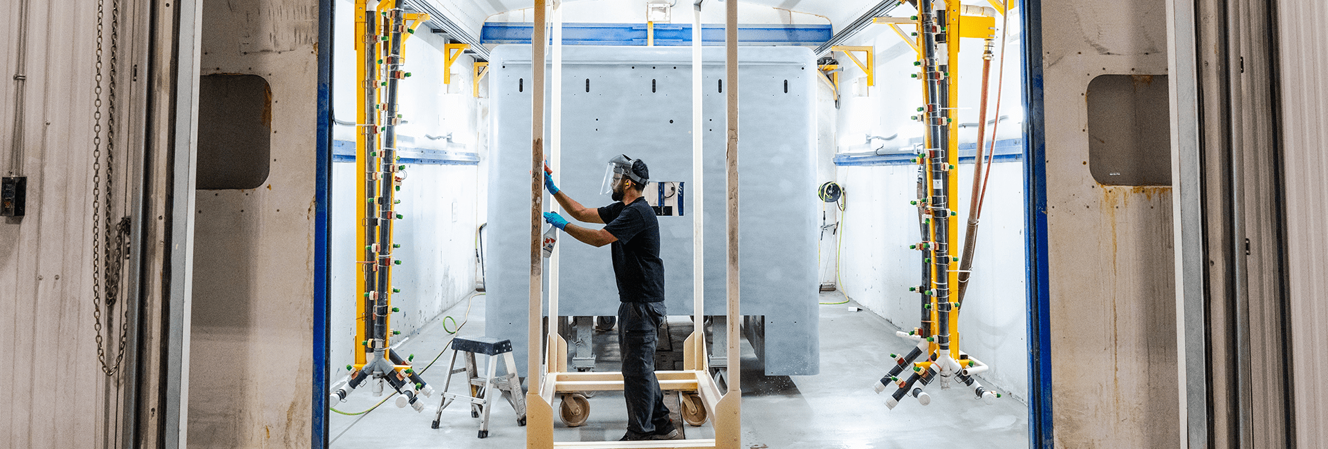 Worker wearing protective gear and gloves prepares an ambulance module for painting inside a controlled spray booth at the Crestline manufacturing facility