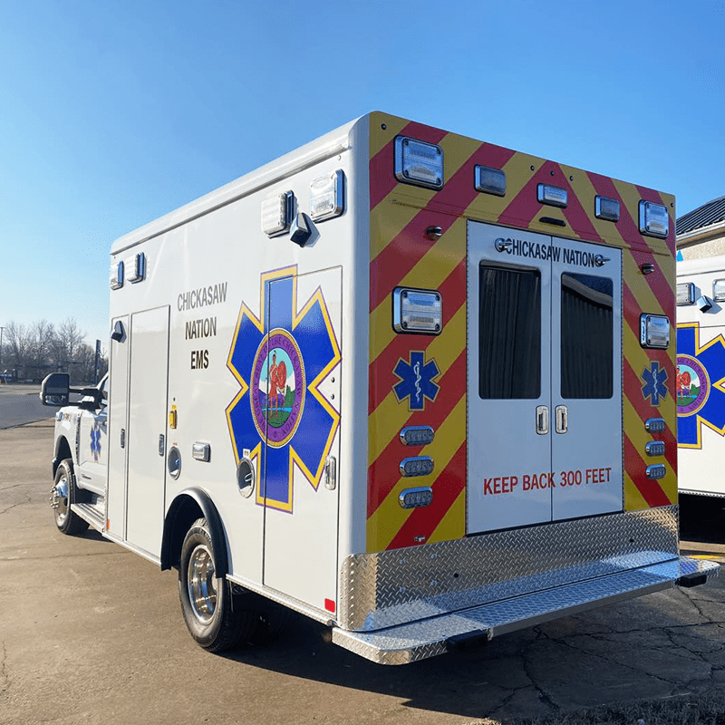 Chickasaw Nation EMS Crestline ambulance with bright red and yellow chevron striping on the back, parked outdoors on a sunny day
