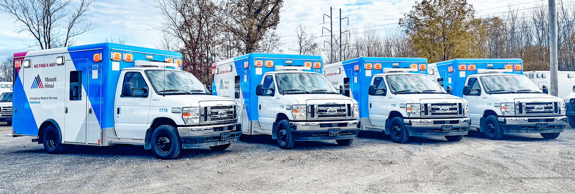 Four Mount Sinai Crestline ambulances with blue and white designs parked in a row outdoors on a gravel lot