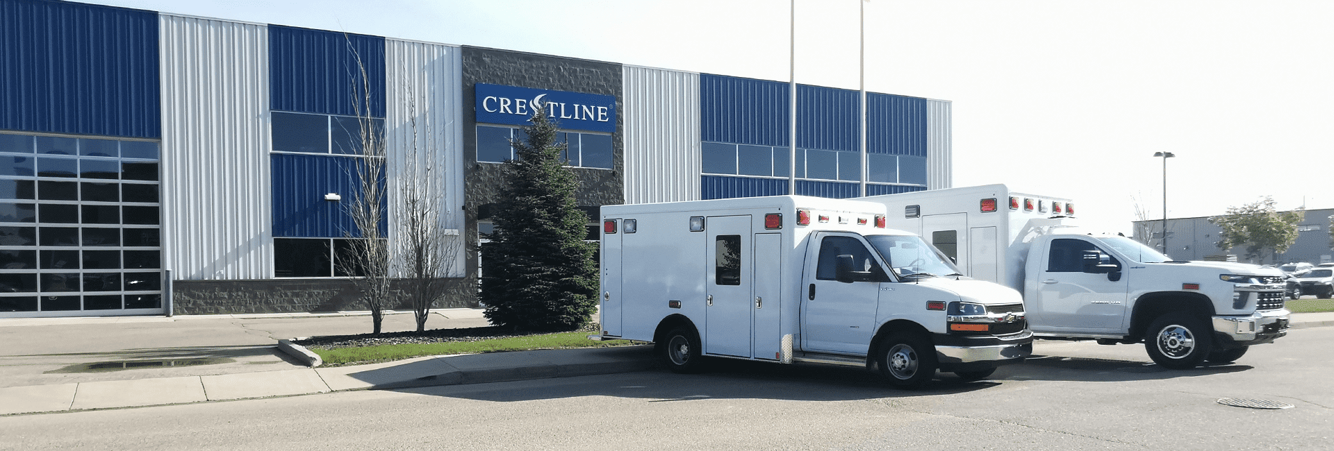 Two white Crestline ambulances parked in front of the manufacturing facility with the company logo visible on the building