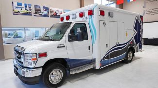 Crestline ambulance on a Ford E-450 chassis, shown indoors with white and blue graphics, red emergency lights, and the Crestline logo