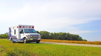 Crestline ambulance on the side of a rural gravel road surrounded by green grass and open fields under a bright blue sky