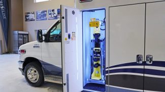 Side compartment of a Crestline ambulance with an integrated yellow oxygen cylinder lift system securely stowed inside, highlighted by bright interior lighting for clear visibility and accessibility