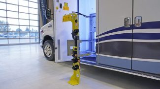 Side compartment of a Crestline ambulance open to reveal a mounted yellow oxygen cylinder bracket system, shown extended for maintenance or access, with interior lighting illuminating the storage area