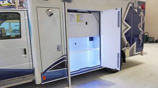 Side compartment of a Crestline ambulance shown open, revealing illuminated shelving and a clean, organized storage space