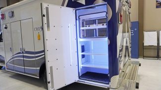 Open rear-side compartment of a Crestline ambulance illuminated with bright LED lighting, showcasing organized interior shelving and durable diamond-plate step surfaces