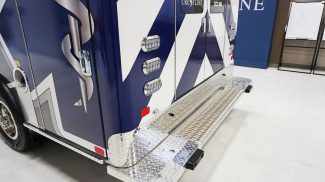 Close-up of the rear exterior of a Crestline CCL 150 ambulance, showing the diamond-plate rear step, bright LED lighting, and sleek blue-and-white graphics featuring the Star of Life design