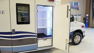 Exterior view of a Crestline ambulance with a side compartment door open, revealing illuminated interior shelving designed for organized storage of medical equipment and supplies