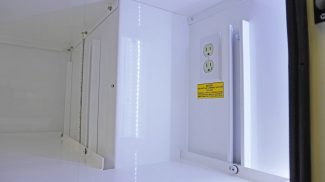 Close-up view of an illuminated Crestline ambulance storage compartment with clean white surfaces, integrated electrical outlets, and a safety notice label
