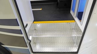 Entry step of a Crestline ambulance featuring diamond plate aluminum flooring with integrated lighting and a yellow safety edge