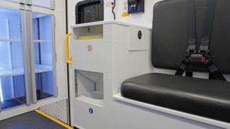 Interior of a Crestline ambulance featuring a black bench seat with seatbelts, a biohazard waste disposal unit, illuminated storage cabinets, and a digital control panel with power outlets