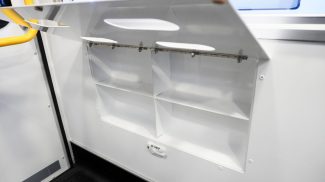 Open lower storage compartment inside a Crestline ambulance, featuring divided shelves and a fold-down access door located beneath the aluminum sliding cabinets