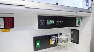 Crestline ambulance interior wall showing the main control panel with touchscreen display, illuminated switches, electrical outlets, oxygen control valves, and onboard suction system for patient care