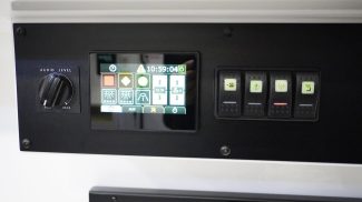 Close-up view of a Crestline ambulance control panel featuring a digital touchscreen interface for lighting and temperature settings, illuminated rocker switches, and an audio level dial