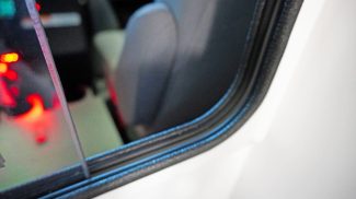 Close-up view through the pass-through window between the cab and patient compartment of a Crestline ambulance, showing part of the seat and illuminated console area with red lighting
