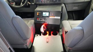 View of the cab console between the driver and passenger seats in a Crestline ambulance, featuring illuminated red lighting, integrated control switches, a touchscreen display, and dual cup holders