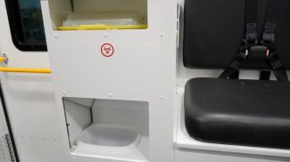 Integrated waste and sharps disposal station inside a Crestline ambulance, featuring clearly labeled biohazard and trash compartments next to a seat with safety restraints