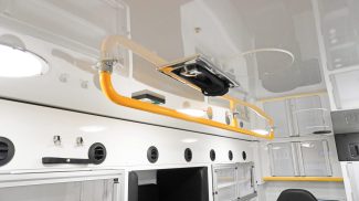 Ceiling-mounted yellow grab rail inside a Crestline ambulance, positioned above upper storage cabinets and air vents for added crew safety and accessibility during transport
