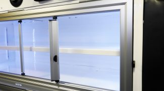 Close-up of an illuminated Crestline ambulance interior cabinet with sliding glass doors, white shelving, and integrated LED lighting along the edges