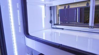 Close-up view of an illuminated Crestline ambulance storage compartment with LED lighting, white shelving, and sliding glass doors framed with black trim