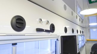 Close-up of Crestline ambulance interior wall featuring multiple round air vents, overhead LED lighting, and illuminated storage cabinets with clear sliding doors and chrome latches