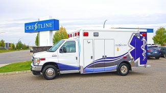 Crestline ambulance parked in front of the Crestline manufacturing facility sign on a clear day