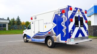 Rear and side view of a Crestline CCL 166 ambulance parked near the Crestline facility, highlighting its bold blue and white graphics and Star of Life design