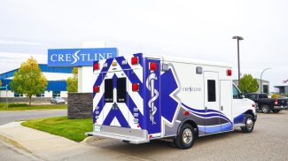 Crestline CCL 166 ambulance parked in front of the Crestline facility sign, showcasing its rear and side graphics under an overcast sky