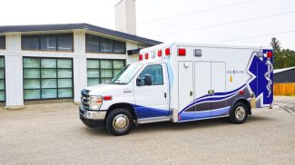 Crestline CCL 166 ambulance parked outside a modern building, featuring a clean white exterior with blue and gray graphics and the Crestline logo on the module side