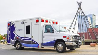 Crestline ambulance parked in an urban setting near a public art sculpture, showcasing its blue and white design with prominent Star of Life graphics