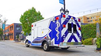 Crestline CCL 166 ambulance parked along a city street, displaying its rear and side graphics with buildings and trees in the background